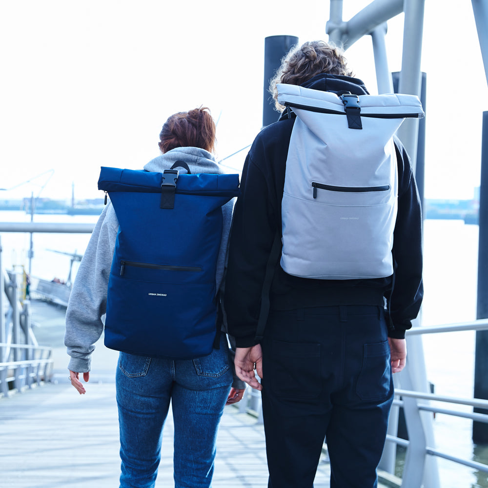 Zwei Menschen haben Rolltop Rucksäcke auf und gehen eine Brücke hinunter
